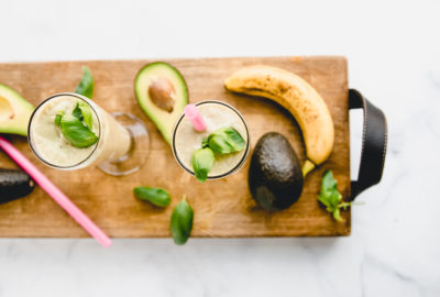 Avocado Basil Morning Smoothie. Made with avocado, basil, banana,pineapple, and coconut milk. Smoothies are on a William Sonoma charcuterie cutting board
