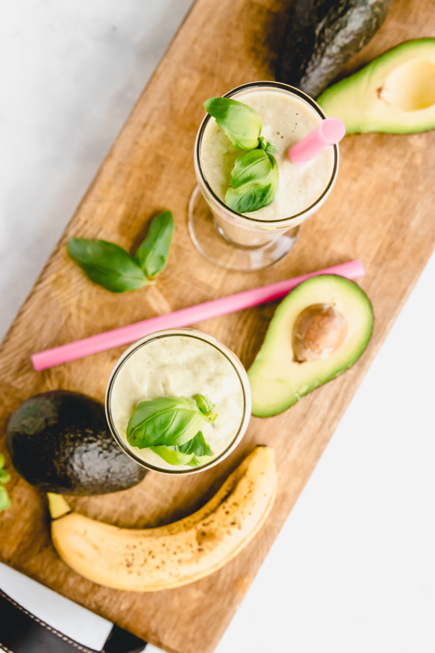 Avocado Basil Morning Smoothie. Made with avocado, basil, banana,pineapple, and coconut milk. Smoothies are on a William Sonoma charcuterie cutting board