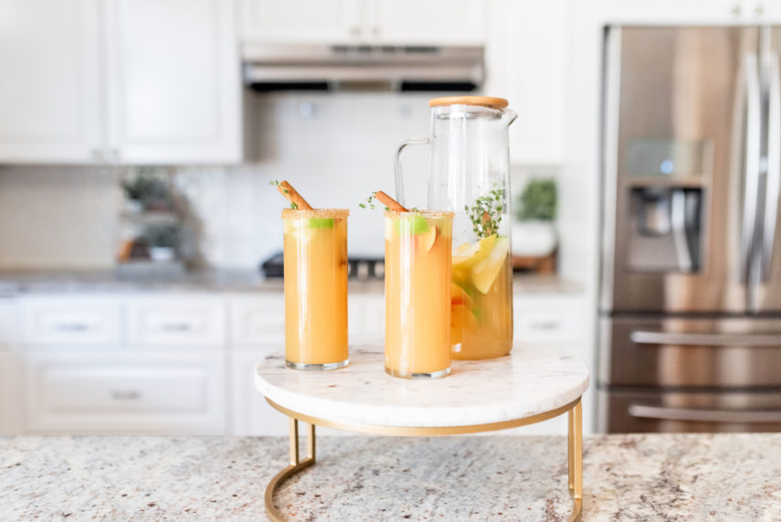 Apple Cider Sangria in clear pitcher with wooden top on marble stand. Sangria in tall glasses with red apples, green apples, and pears with sugar rim. Apple cider sangria food photography