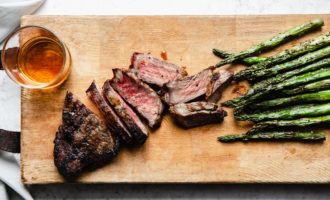 grilled steak cut into strips on a wooden bard with whiskey glass and asparagus on the side