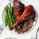 over head shot of smoked turkey legs on circular white plate with green beans and grains.