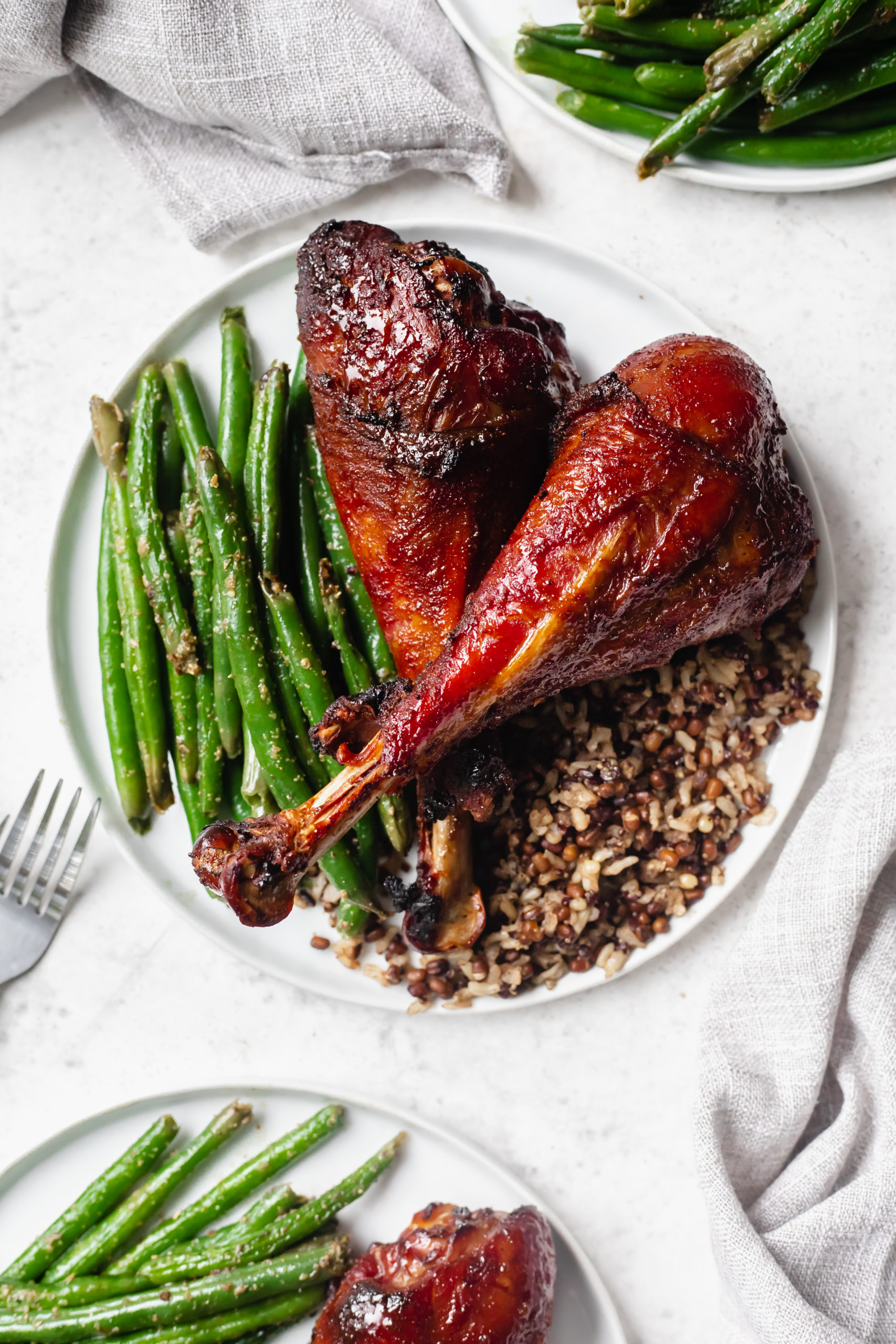 overhead shot of smoked turkey legs on circular white plate with green beans and farro. 